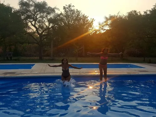 Dos chicas saltan en la pileta al atardecer, con el sol entre los árboles