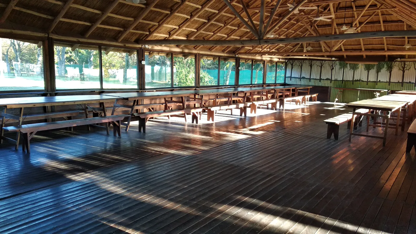 El Quincho 5 por dentro: piso de madera, techo alto y mesas largas